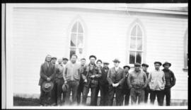 Group portrait of men posed beside a church