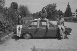 [Isaac, Ron and Chip sit on top of car]