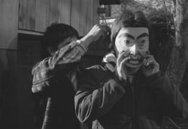 [Norman Tait assists unidentified person with mask]