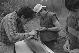 [Chip, Isaac and Norman adjusting model canoe]