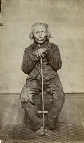 [Portrait of man seated with cane]