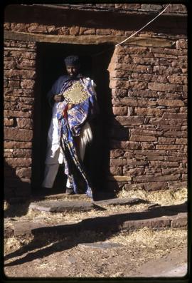 Priest in the entrance of a rock church with gold cross