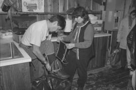 [Reva Robinson assists Norman Tait in carving hut]