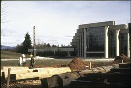 Two men stand near poles for the Haida and mortuary houses