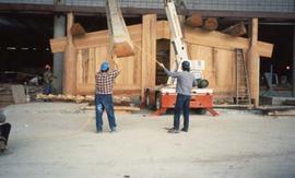 Two men standing in front of a longhouse