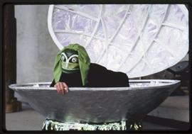 A performer in a frog mask in a shell